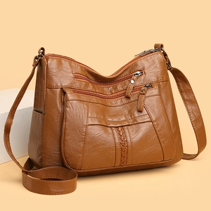 Detail view of brown soft leather crossbody bag featuring multiple zipper pockets and braided trim