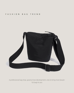 Detail of black nylon bucket bag featuring a minimalist logo and adjustable wide strap