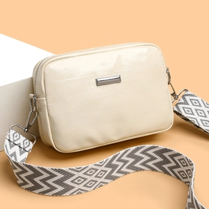 Minimalist silver textured crossbody bag with geometric wide strap on a white stand
