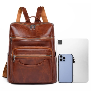 Brown faux leather backpack with leaf texture and multi-pocket design next to a tablet