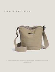 Detail view of khaki nylon bucket bag showing multiple zippers and adjustable strap