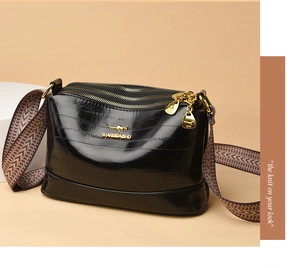 Detailed view of the shiny black leather crossbody bag with triple zipper and knit strap