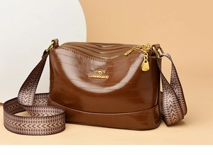 Detail of a brown leather crossbody bag with three zippers and a colorful woven strap