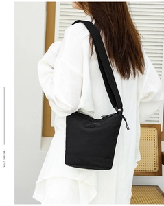 Detailed side view of a black nylon bucket bag with a branded strap shown on a model