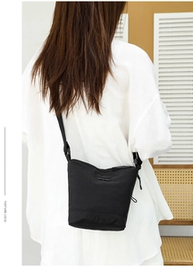 Detail of adjustable nylon strap and metal hardware on the black bucket shoulder bag