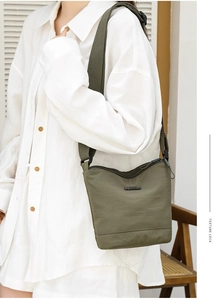 Detail of dark green nylon bucket bag featuring a wide strap and minimalist branding