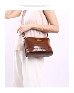 Detail of dark brown faux-crocodile shoulder bag with golden logo and woven strap