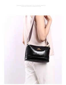 Detail view of glossy black crossbody bag with golden logo and wide patterned strap