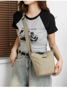 Detail of beige nylon bucket bag featuring a black logo badge and adjustable wide strap