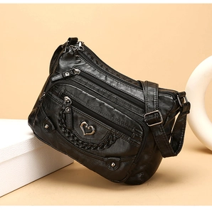 Dettaglio borsa a tracolla nera con zip multiple e fibbia decorativa in metallo a cuore