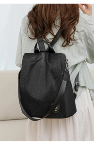 Rear view of a black waterproof Oxford cloth backpack worn by a female model in a room