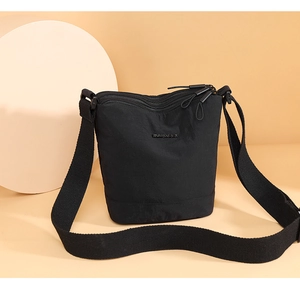 Detail view of adjustable wide shoulder strap and brand plate on black nylon bucket bag