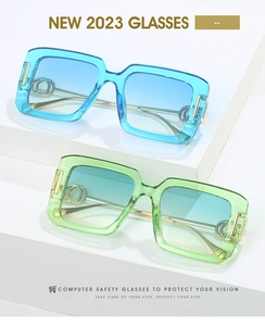 Close-up of square glasses with gold double-ring hinge detail and gradient blue-green lenses