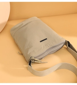 Close-up of light khaki nylon bucket bag showing multiple zippers and wide fabric strap