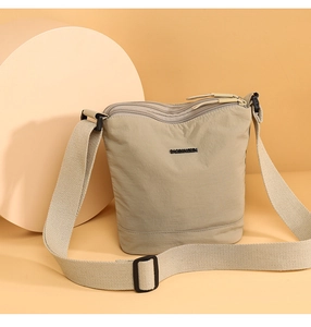 Detail view of the multi-layer zipper pockets on a beige nylon bucket crossbody bag