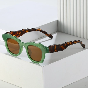 Women's trendy sunglasses with green wavy frames and tortoiseshell temples on white stand