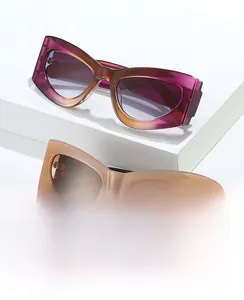 Détail de lunettes de soleil œil-de-chat dégradé violet et beige sur socle blanc