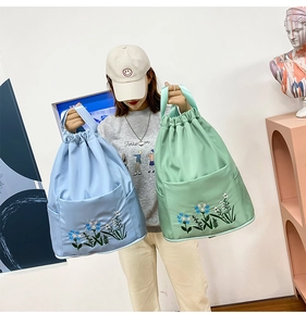 Detail of floral embroidery on water-resistant nylon drawstring backpacks in blue and green