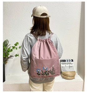 Pink oxford backpack with floral embroidery detail and drawstring closure shown on model