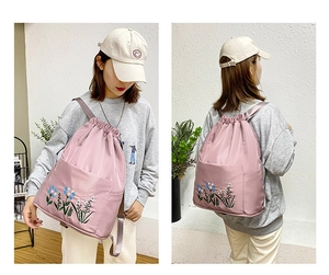 Detail of pink oxford backpack featuring floral embroidery and large front storage pocket