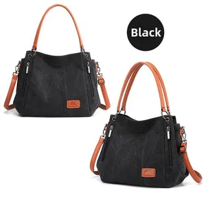 Close-up of black canvas tote bag with brown leather handles and side silver zipper detail