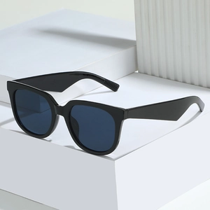 Minimalist black oversized sunglasses with thick frames and dark blue lenses on white blocks