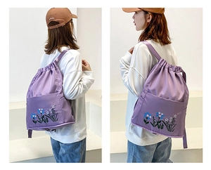 Detail of purple nylon drawstring backpack with floral embroidery and open front pocket