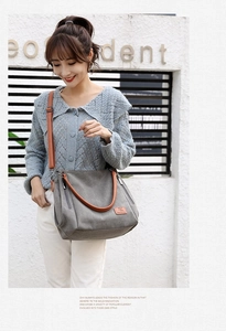 Gray canvas tote bag featuring brown leather straps and side zipper details worn by model