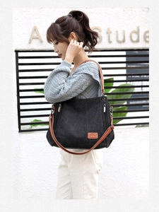 Detail of a large black canvas tote bag with brown leather handles and side zipper pocket