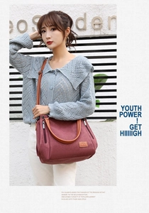 Detail of burgundy canvas tote bag showing brown leather handles and side zipper pocket