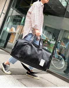 Detail of black leather travel bag showing side logo and adjustable shoulder strap