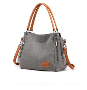Detail of gray canvas tote with brown leather handles and side zipper pockets