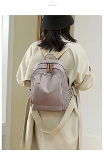 Detail of grey-purple nylon backpack with leather zipper pulls on a female model
