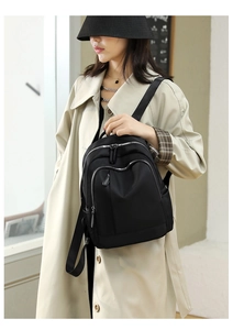 Detail of black oxford backpack with silver zippers on a stylish beige trench coat