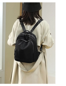 Rear view of black oxford fabric backpack with silver zippers on model's back