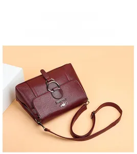 Detail of burgundy lychee grain leather crossbody bag with metal ring buckle and logo