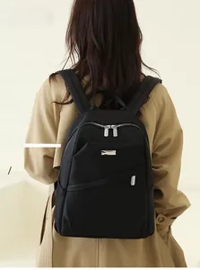 Vue de dos d'un sac à dos noir en nylon imperméable sur un modèle en trench-coat kaki