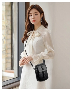Detail of minimalist black PU leather crossbody bag with metallic buckle on white shirt