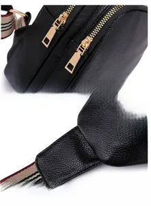 Detail of black pebbled leather chest bag with golden zippers and striped strap
