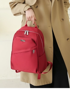 Détail du sac à dos oxford rouge avec zips argentés porté avec un trench-coat beige