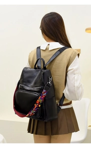Detailed back view of a black leather backpack with a colorful woven shoulder strap