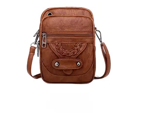 Detail view of brown textured leather phone bag with multiple zippers and woven charms