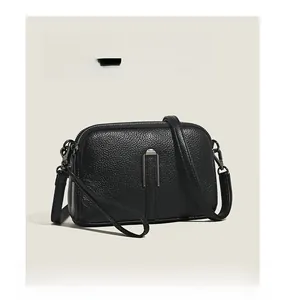 Detail of black pebbled leather crossbody camera bag with silver metal clasp and zipper