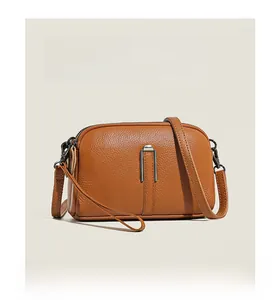 Close-up of litchi grain cowhide leather and gunmetal zippers on a brown crossbody bag