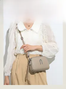 Detail of taupe litchi grain leather crossbody bag with multiple zipper layers and metal trim