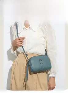 Detail of light blue genuine leather crossbody bag with pebble texture and silver buckle