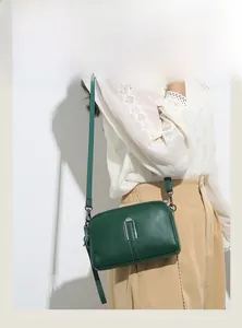 Detail of green litchi leather crossbody bag with dual zippers and woven shoulder strap