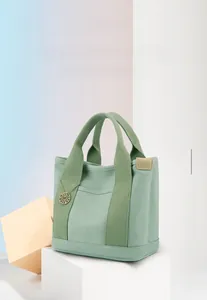 Detailed view of canvas handbag with leather trim and decorative metal initial charm