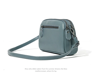 Detail of blue pebbled leather crossbody bag showing multi-zip layers and textured cowhide