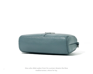 Detail view showing pebbled cowhide leather texture and stitching on gray-blue small bag